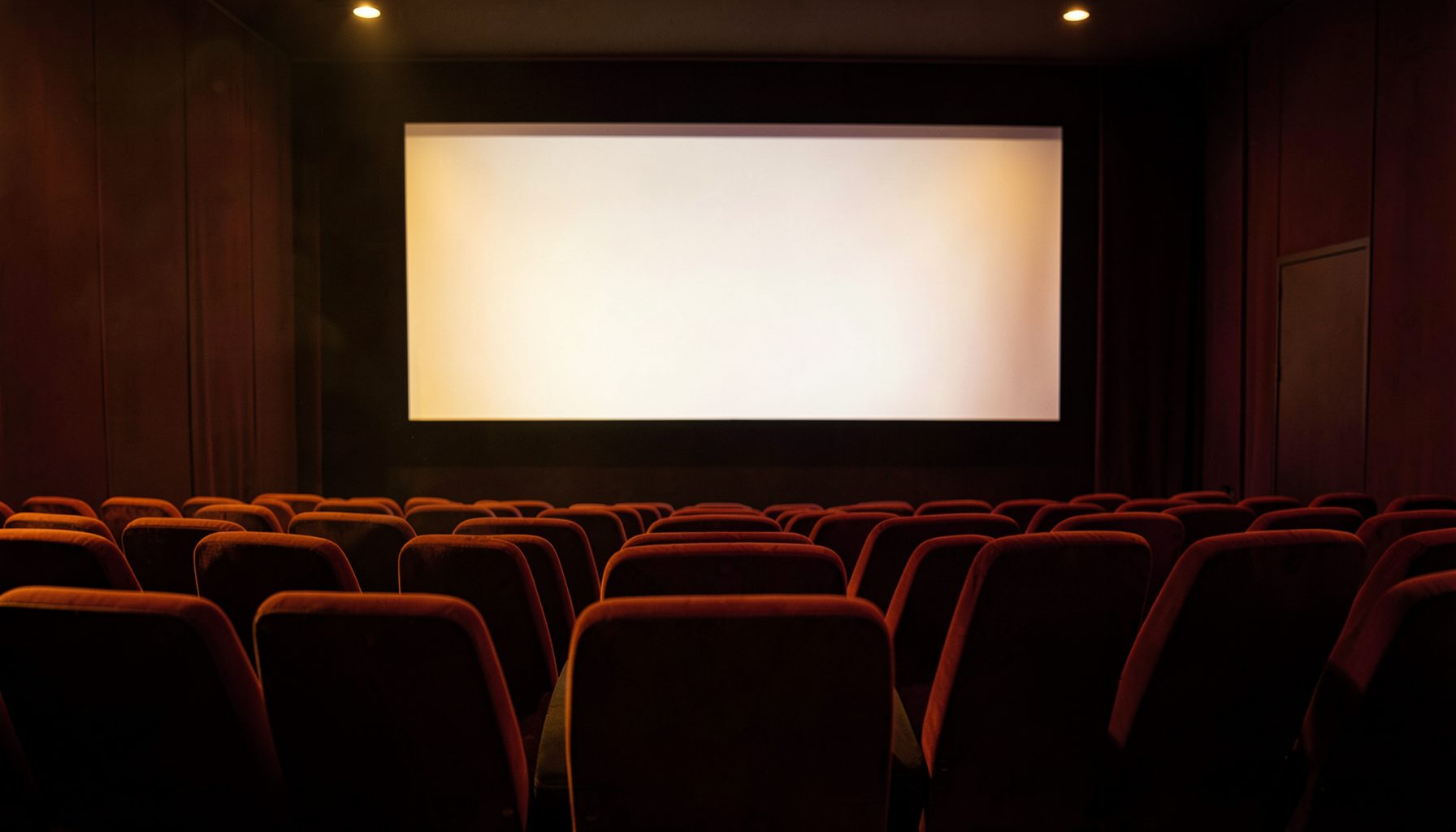 Une salle de cinéma vide baignée d'une lumière tamisée dorée et rouge, les fauteuils en velours alignés en courbe douce